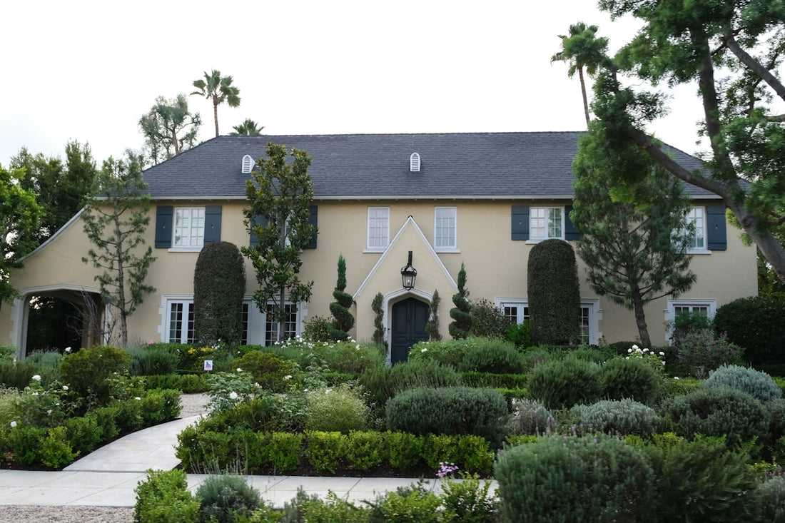 A large tan house with manicured gardens and palm trees