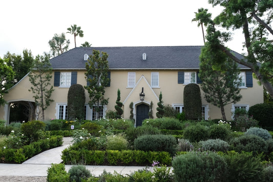 A large tan house with manicured gardens and palm trees