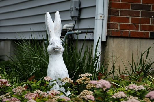 A white rabbit garden statue amongst pink flowers