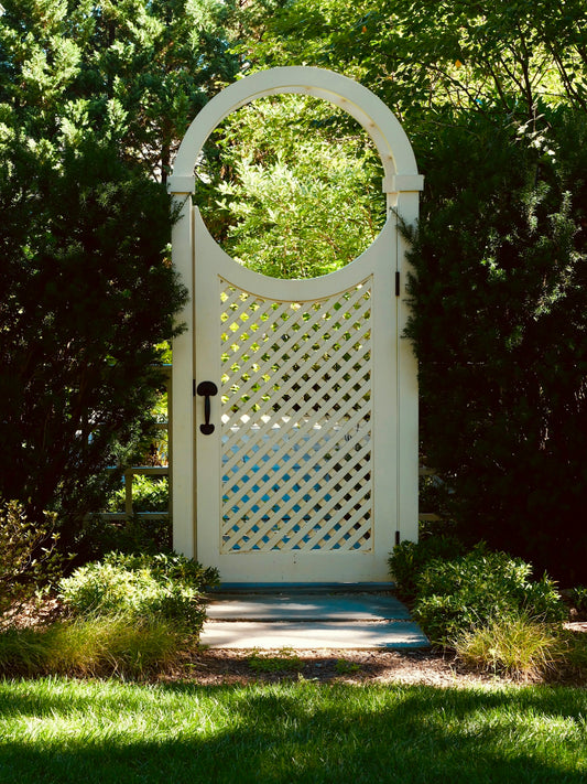 White lattice garden gate with circular top surrounded by greenery